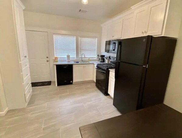Compact kitchen with oven, microwave, and refrigerator, featuring a tiled floor and two windows.