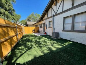 Enjoy a serene backyard with artificial turf, a wooden fence, and a shaded setting.