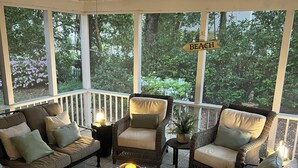 Eine überdachte Terrasse mit Korbmöbeln, einem Glastisch und einem Deckenventilator.