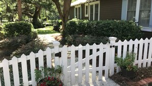 Ein Wohnhaus mit weißem Zaun, Kiesweg und einem gepflegten Garten mit verschiedenen Pflanzen und Blumen.