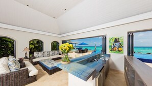 A modern kitchen with a large island, a dining area with outdoor seating, and a view of the ocean.
