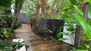 A wooden pathway surrounded by lush greenery and a stone planter.