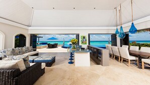 A spacious living area with a view of the ocean, a bar area, and a seating arrangement with a pool view.