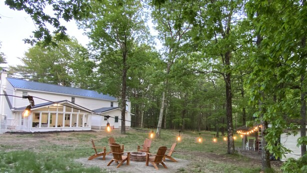 Un patio trasero con un brasero, mobiliario exterior e iluminación con luces colgantes.