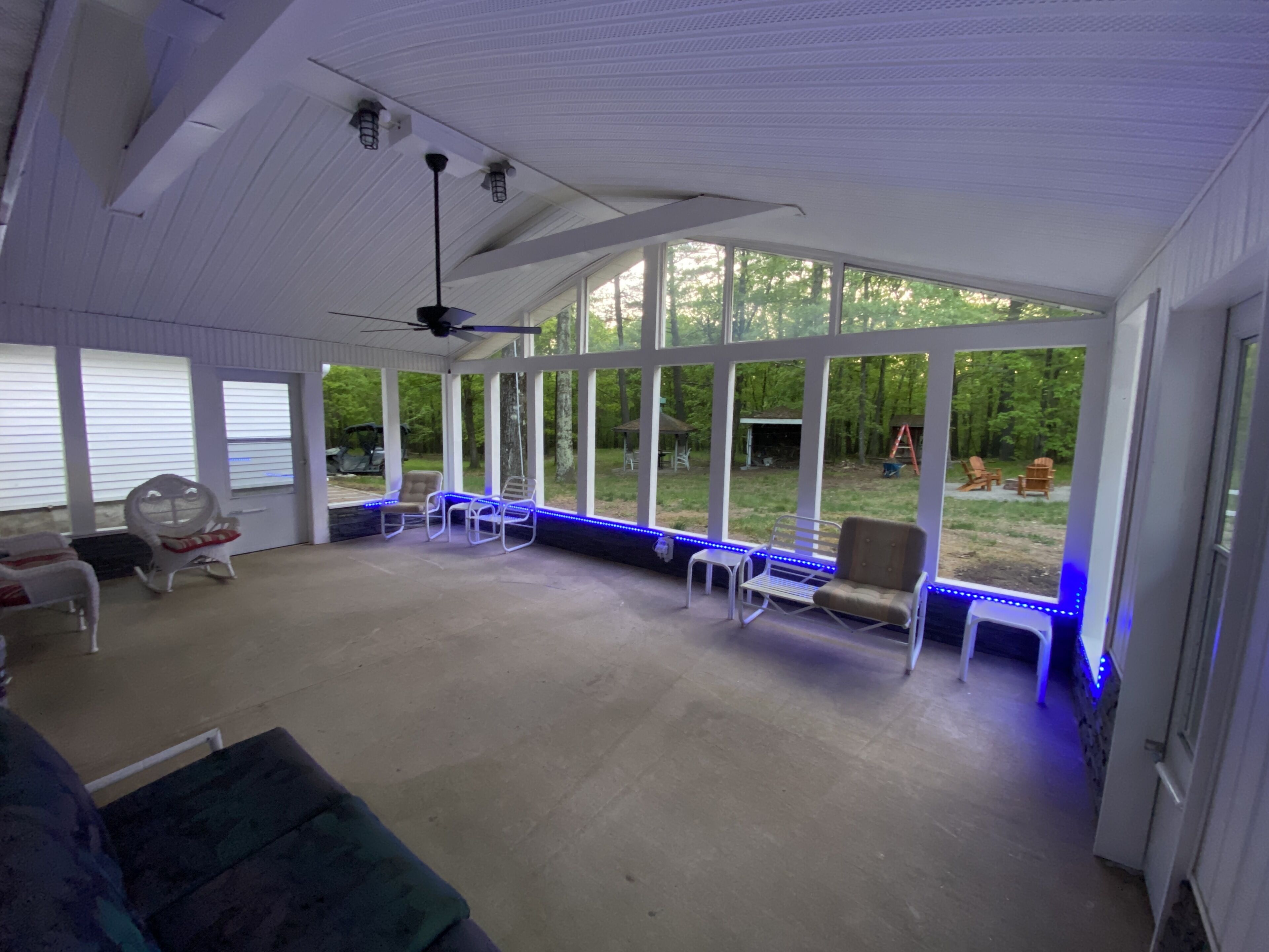 Eine überdachte Terrasse mit Deckenventilator, großen Fenstern und Sitzgelegenheiten im Freien.