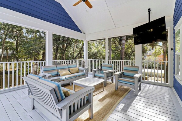 Relax in this serene outdoor space with a sofa, chairs, and flat-screen TV, surrounded by lush views of the surrounding trees.