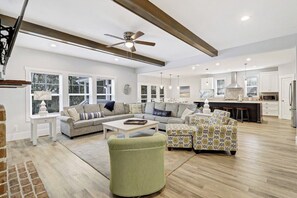 Relax in this spacious living room with a high ceiling and exposed beams, featuring a large sectional sofa, armchair, and ottoman.