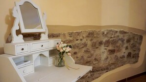 Ein weißer Waschtisch mit Spiegel und Schubladen, eine Vase mit Blumen und eine Steinwand.