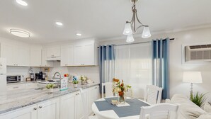 Een moderne keuken met witte kasten, een marmeren aanrecht en een eethoek met een tafel voor vier personen.