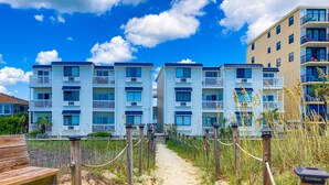 Een gebouw aan het strand met meerdere balkons en een zandpad dat naar de ingang leidt.