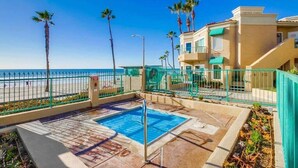 A pool area with a clear view of the ocean, surrounded by a fence and palm trees. - Beachfront Luxury 2BR with Ocean-View Balconies & Spectacular Sunsets (Oceanside)