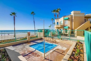 A pool area with a clear view of the ocean, surrounded by a fence and palm trees. - Beachfront Luxury 2BR with Ocean-View Balconies & Spectacular Sunsets (Oceanside)