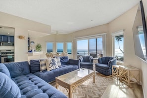 A spacious living room with a large sectional sofa, a coffee table, and a view of the ocean.