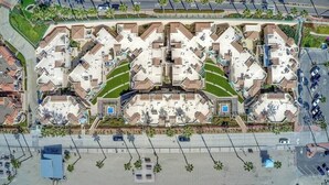An aerial view of a residential complex with multiple apartment buildings, a central courtyard, and a beach area. - Beachfront Luxury 2BR with Ocean-View Balconies & Spectacular Sunsets (Oceanside)