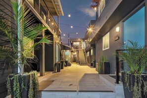 Un edificio moderno con una escalera que conduce a un nivel superior, rodeado de plantas en macetas y luces colgantes.