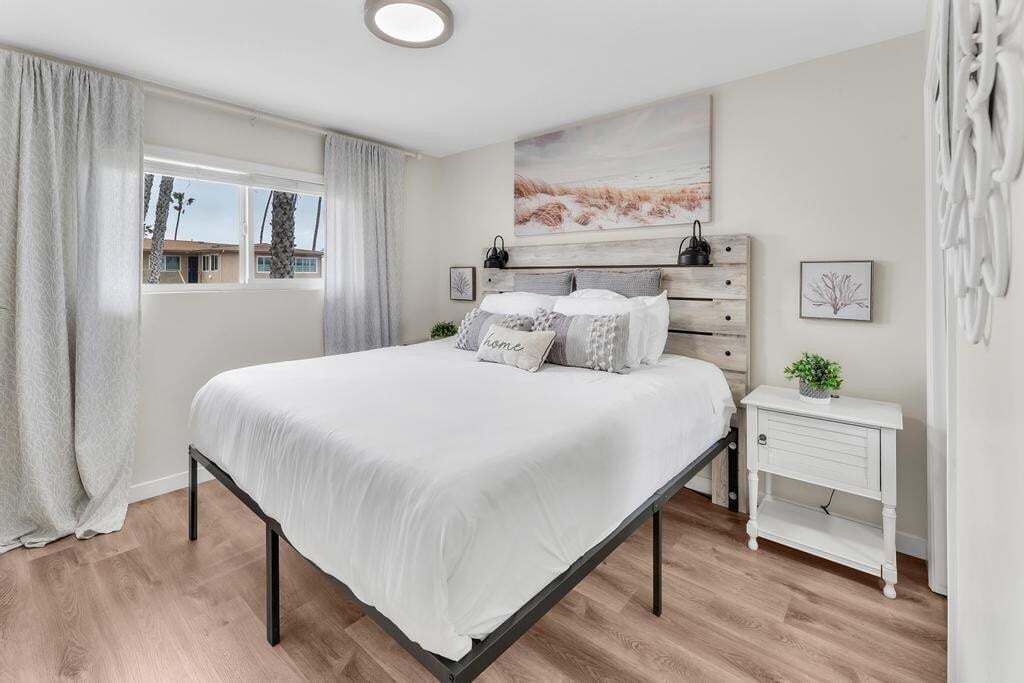 Une chambre à coucher avec un lit, une table de chevet, une fenêtre avec des rideaux et un tableau au mur.