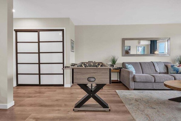 Una sala de estar moderna con piso de madera, un sofá gris, una mesa de centro y una mesa de fútbol.