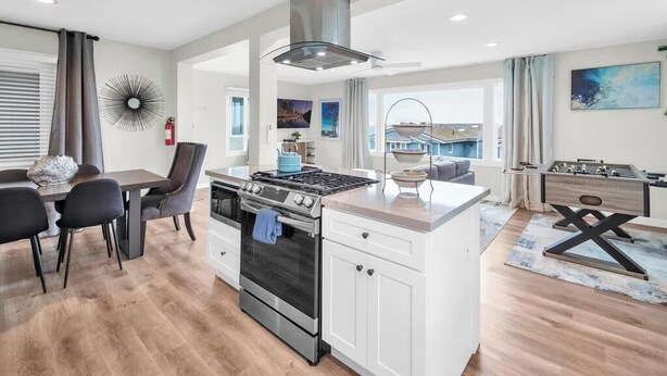 A modern kitchen with a central island, a dining area with a table and chairs, and a view of the outside.