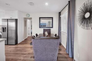 A modern kitchen with stainless steel appliances, a dining area with a dark wooden table and grey upholstered chairs, and a decorative mirror on the wall. - Coastal Comfort | Tower 9 Condo w/ Ocean Views (Oceanside)