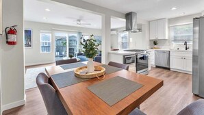A modern kitchen with white cabinets, stainless steel appliances, and a dining area with a wooden table and chairs. - Oceanview Escape | Tower 9 Condo Steps from the Beach (Oceanside)