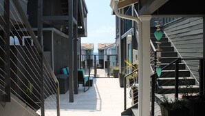 A narrow outdoor corridor with a staircase on the right, a bench, and potted plants. - Oceanview Escape | Tower 9 Condo Steps from the Beach (Oceanside)