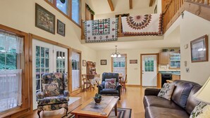 A spacious living room with a high ceiling, wooden beams, and large windows. There are two sofas, a coffee table, and a fireplace. - Clean One Bedroom plus Loft Bedroom Two Bath Cottage with Wi-Fi & Pool Access. (Townsend)