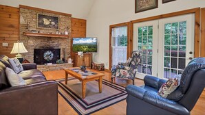 A living room with a fireplace, a television, a sofa, a chair, and a view through the glass doors. - Clean One Bedroom plus Loft Bedroom Two Bath Cottage with Wi-Fi & Pool Access. (Townsend)