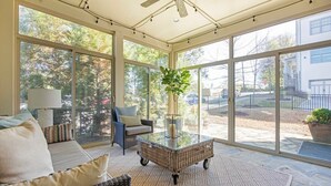 Une véranda avec de grandes fenêtres, des meubles en osier et une table basse en verre.