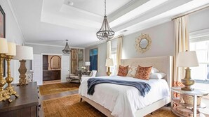 Une chambre spacieuse avec un grand lit, un lustre et une vue sur la ville.
