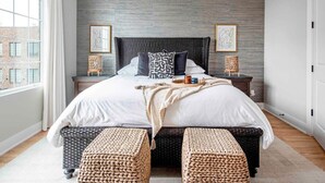 A modern bedroom with a large bed, two side tables, wicker ottomans, and artwork on the walls. - Sky's the Limit (Atlanta)