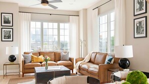 A modern living room with a brown leather sofa set, a coffee table, and a view of the city through large windows. - Sky's the Limit (Atlanta)