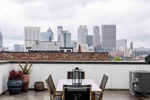 Terraço no telhado com mesa, cadeiras, plantas em vasos e um aparelho de ar condicionado.