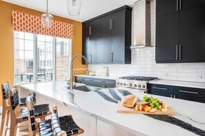 A modern kitchen with black cabinets, a large island, and a window overlooking a cityscape. - Bird's Eye View (Atlanta)
