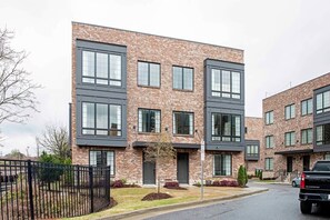 A multi-story residential building with a brick facade, large windows, and a black fence in the foreground.