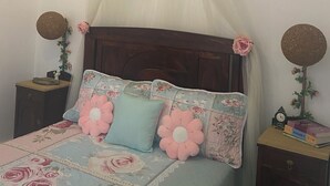A bedroom with a canopy bed, floral bedding, two nightstands with decorative items, and a wooden headboard.