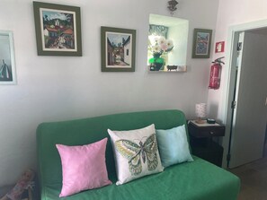 Una habitación con un sofá cama verde, dos almohadas, un extintor y cuadros en la pared.