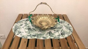 A wooden table with a floral-patterned tablecloth and a decorative bowl with a handle.