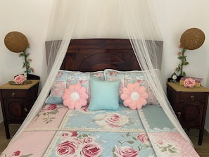 Un lit avec une couvre-lit à motifs floraux, un baldaquin et des coussins décoratifs.