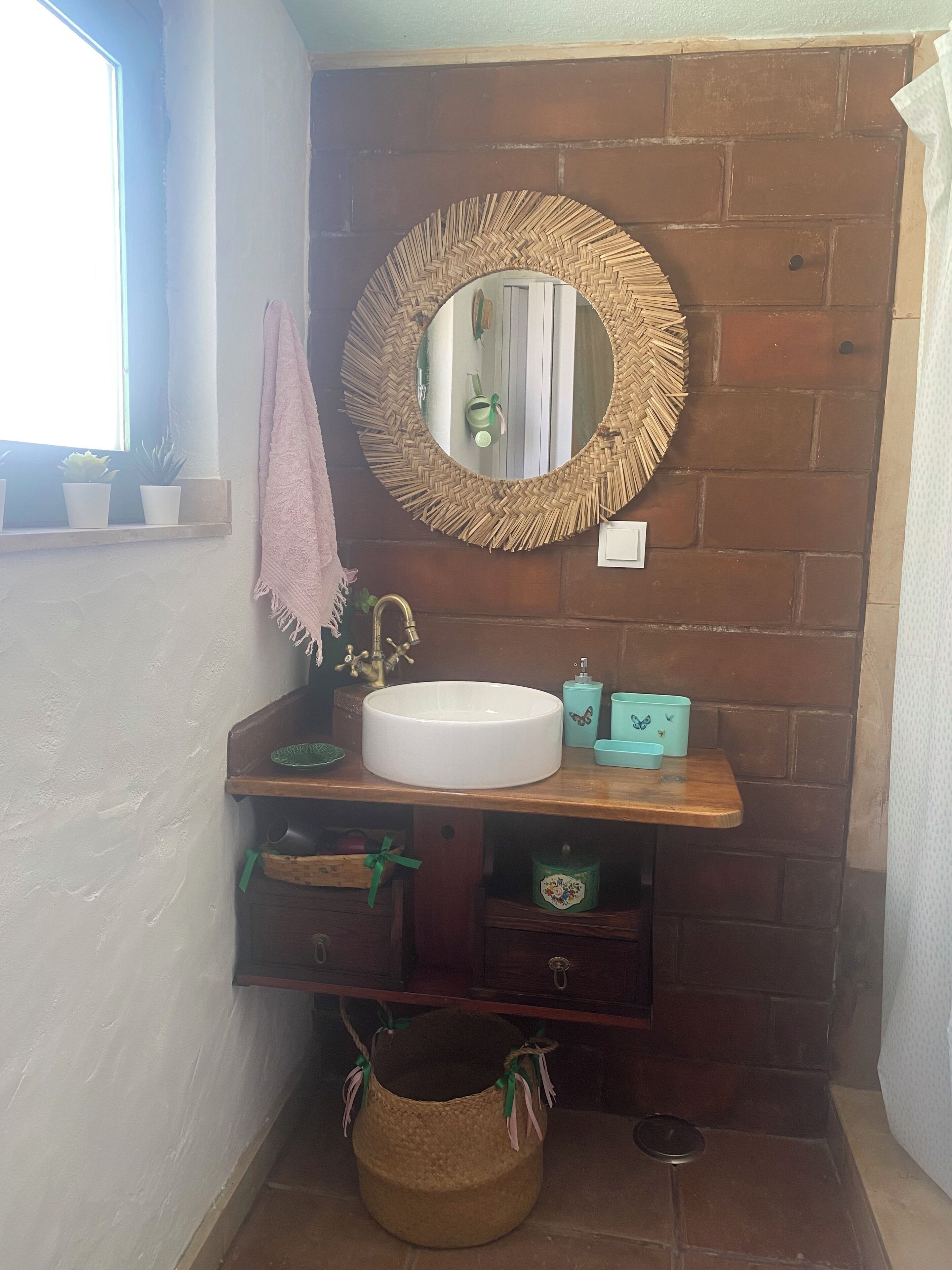Une salle de bain avec un miroir rond, un lavabo blanc, un meuble-lavabo en bois et une petite fenêtre.