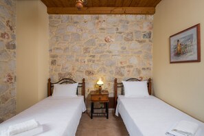 Una habitación con dos camas individuales, una pared de piedra, techo de madera y un cuadro en la pared.