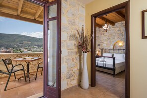 Un balcón con una mesa y sillas, un muro de piedra y una cama en la habitación contigua.