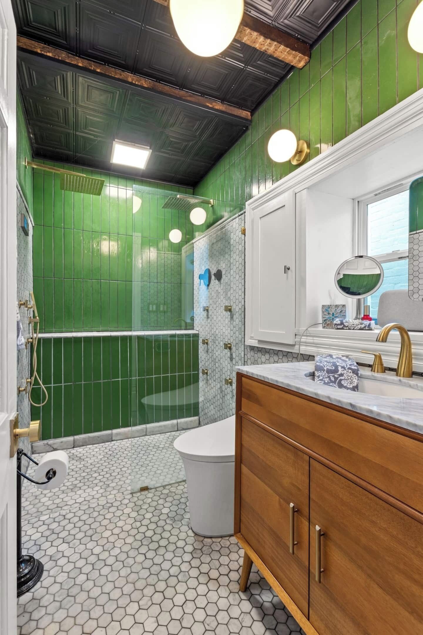 Un bagno con pareti verdi, un water bianco, un mobile bagno in legno con un rubinetto dorato e uno specchio sopra il lavandino.