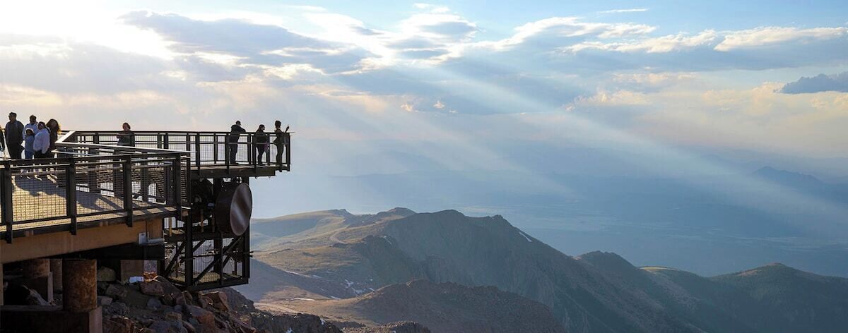Eine Aussichtsplattform mit Metallgeländer, das auf eine Berglandschaft blickt.