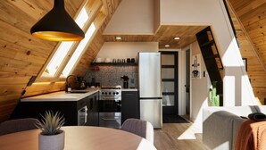 A modern loft-style kitchen with a wooden ceiling, skylight, and a dining area with a round table and chairs. - Elwood's A-frame · Modern A-frame w/ hot tub + view (Florissant)