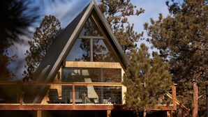 A modern cabin with a large glass window, surrounded by trees. - Elwood's A-frame · Modern A-frame w/ hot tub + view (Florissant)
