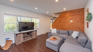 Ein modernes Wohnzimmer mit einer großen Eckcouch, einem Flachbildfernseher auf einer Holz-Unterhaltungsecke und einer Holztreppe.