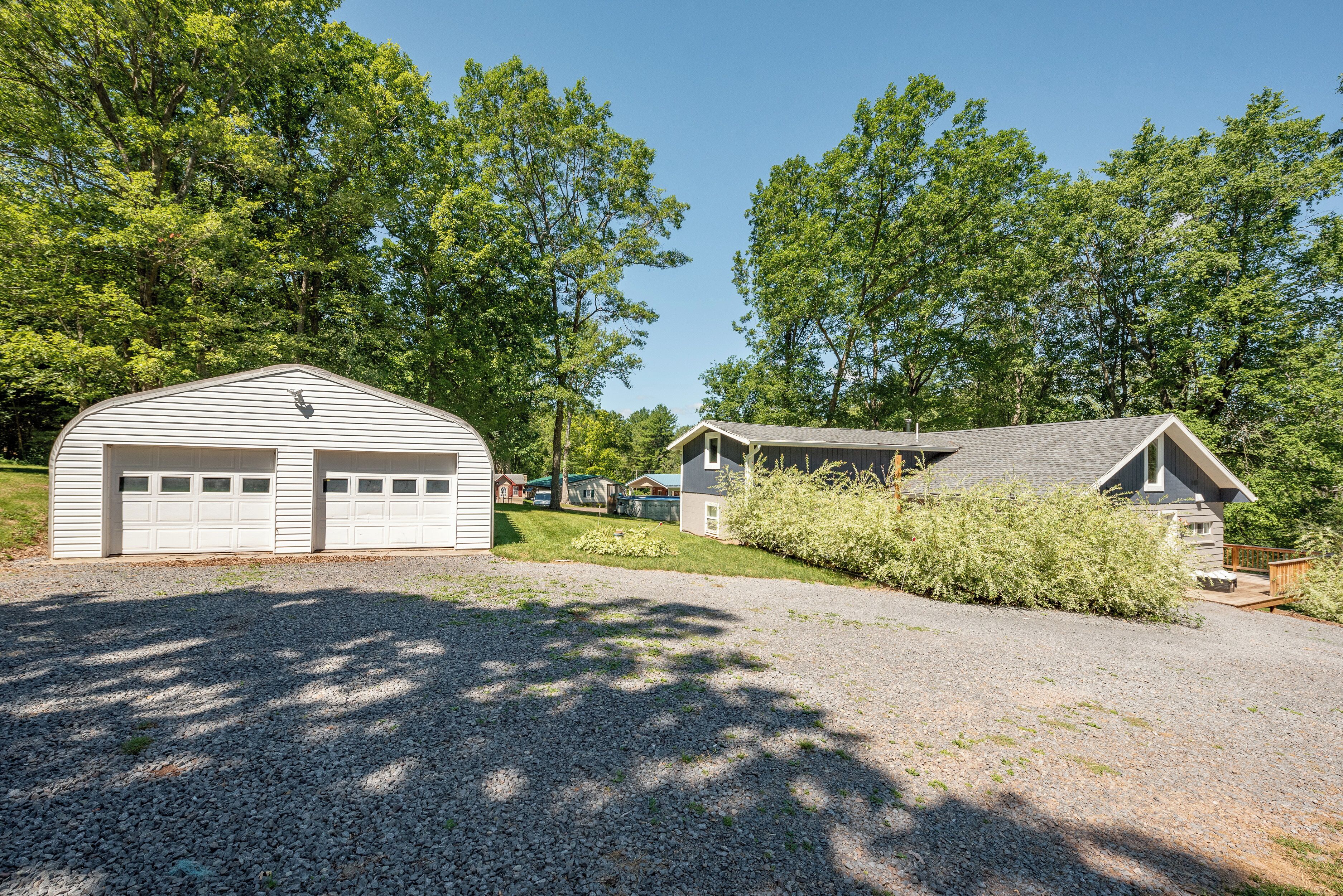 A two-story building with a garage and a shed, surrounded by trees and a gravel driveway.