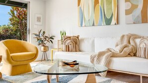 A modern living room with a white sofa, a yellow armchair, a glass coffee table, and abstract wall art. - Cool, Lo-Fi Styled Surf Shack - Ka Hale Nalu (Princeville)