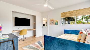 Un dormitorio moderno con una cama azul, un escritorio con silla, un televisor de pantalla plana y una ventana con vistas a zonas verdes.