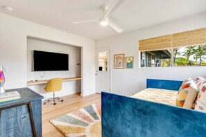 Une chambre moderne avec un lit bleu, un bureau avec une chaise, un téléviseur à écran plat et une fenêtre donnant sur un paysage verdoyant.